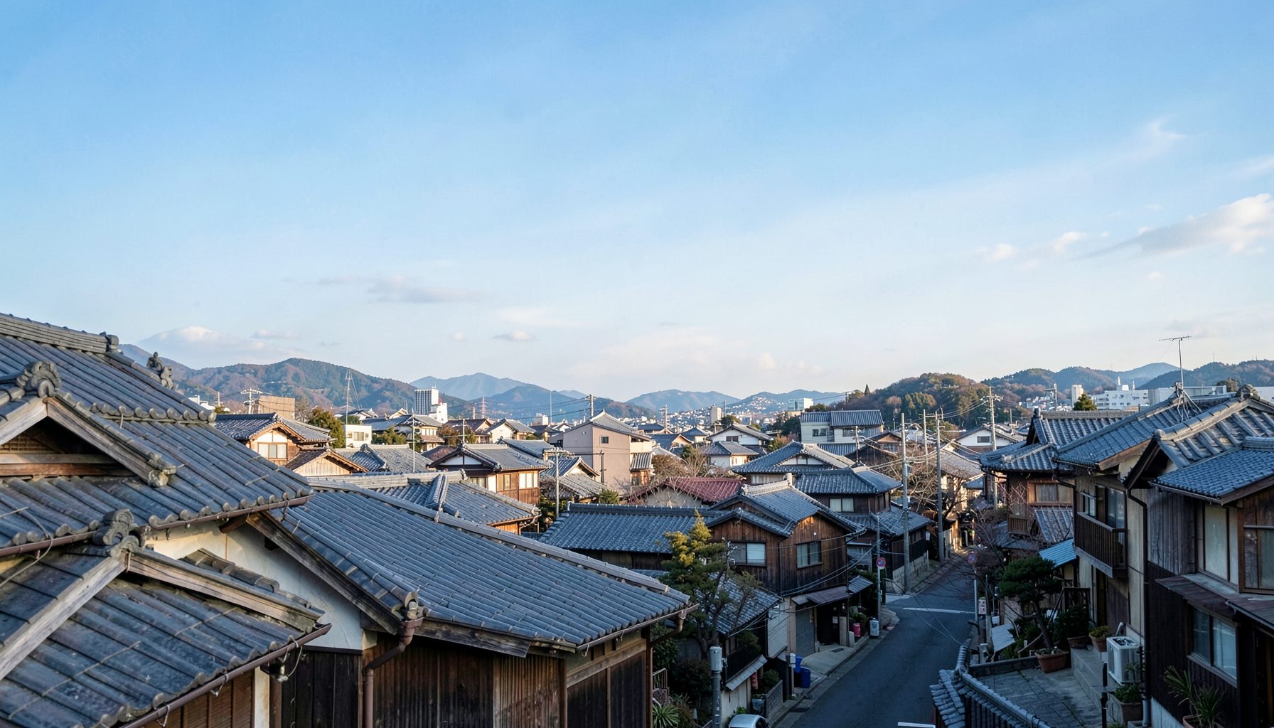 Aerial view of a traditional tiled-roof neighborhood with mountains in the distance under a clear blue sky, warm daylight
