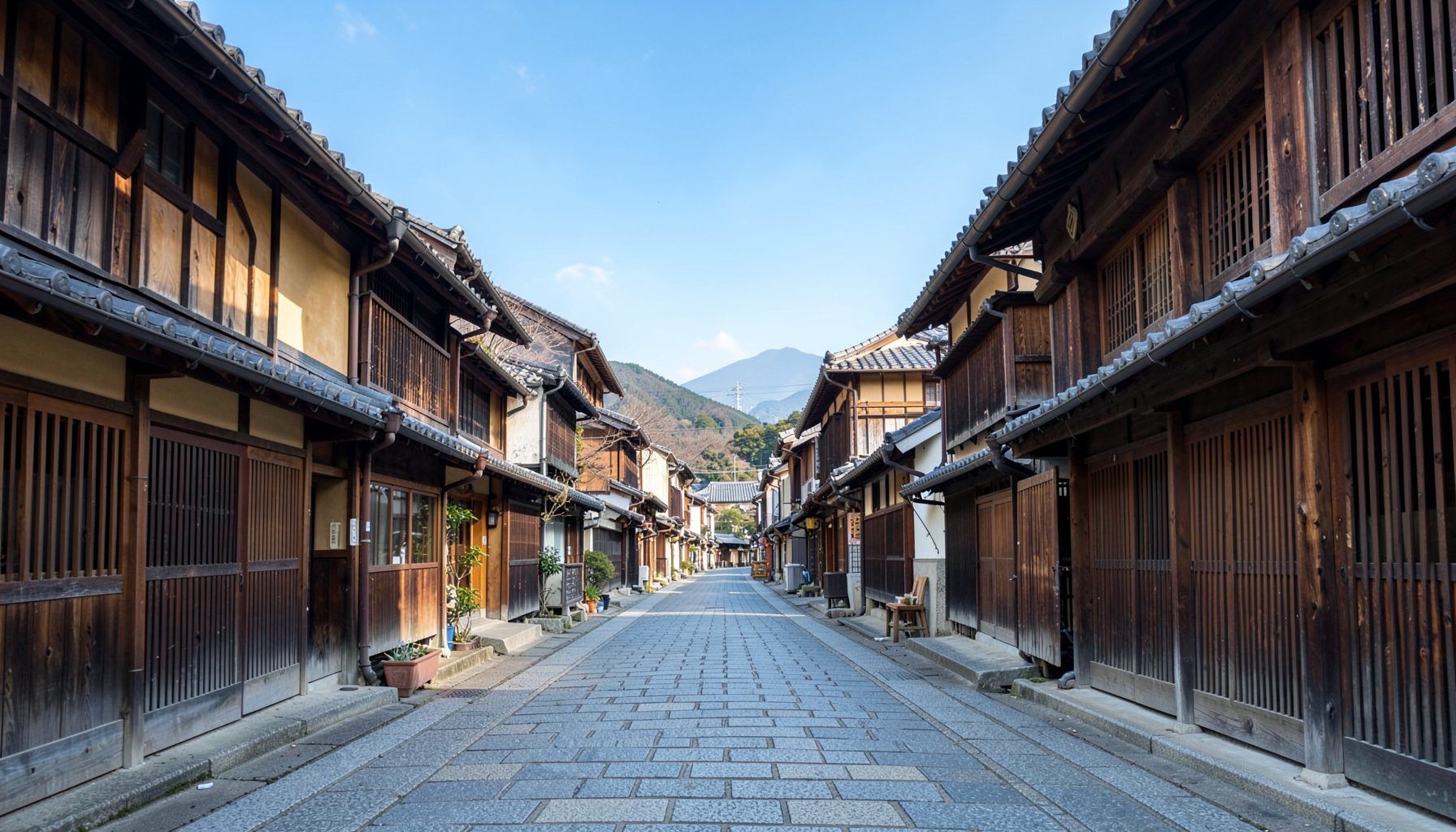 Empty stone-paved street lined with traditional wooden buildings, mountains visible in the distance, warm daytime mood