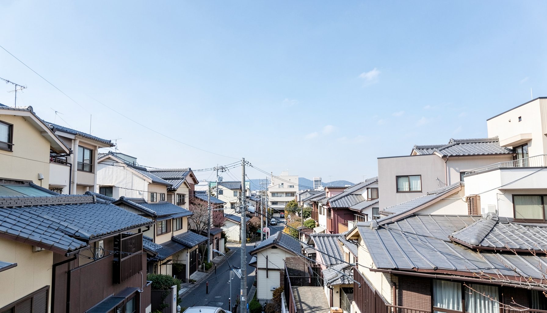 Elevated view of a dense residential neighborhood with tiled roofs and utility poles under a clear blue sky, calm daytime